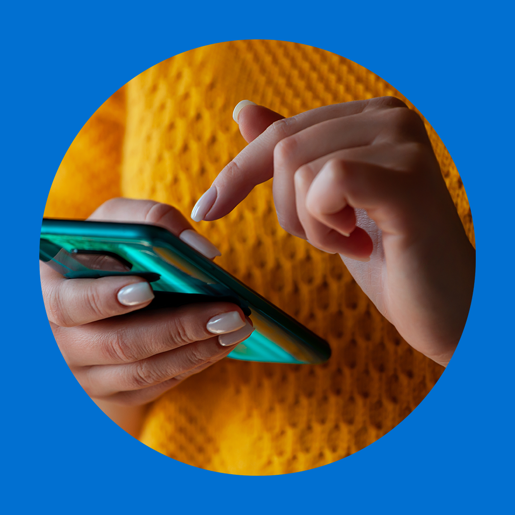 Inimene udustatud näoga hoiab nutitelefoni, istudes laua taga, millel on kollaste lillede vaas; taustal on köögikapid