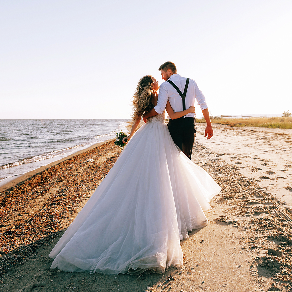 Свадебная пара держится за руки на пляже